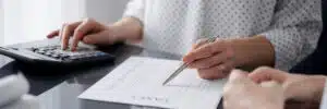 Woman using a calculator and laptop computer while counting property taxes for a client.